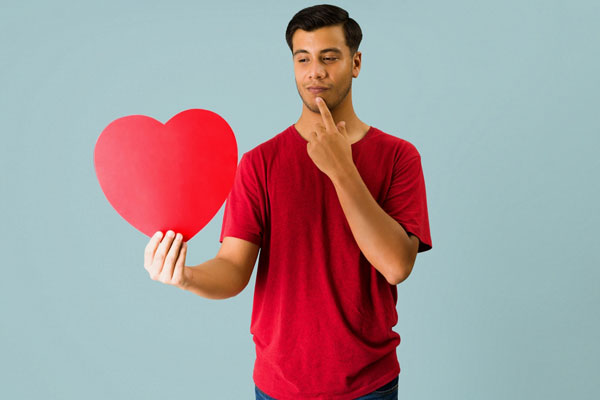 A man holding a paper heart with a questioning look